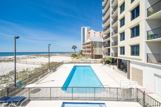 community pool featuring a water view, a patio area, fence, and a view of the beach