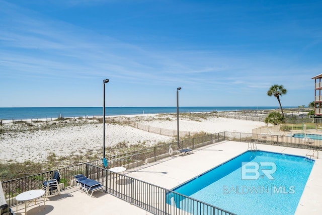 community pool with a water view, fence, and a beach view