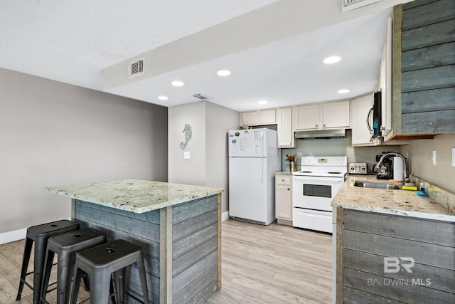 kitchen featuring white appliances, visible vents, light stone counters, under cabinet range hood, and a kitchen bar