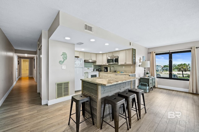 kitchen with under cabinet range hood, white appliances, visible vents, light wood-type flooring, and light stone countertops