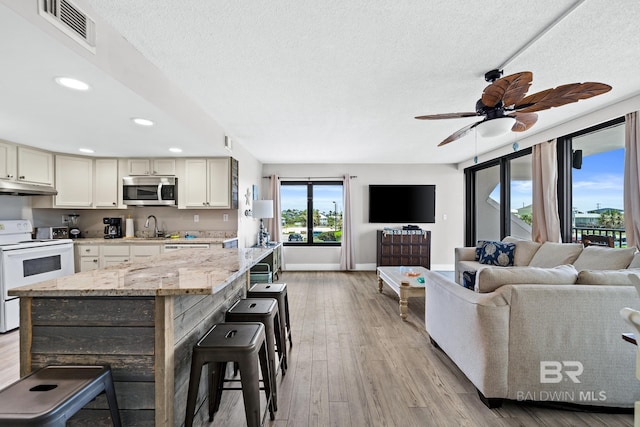 kitchen with under cabinet range hood, white electric range, a breakfast bar, open floor plan, and stainless steel microwave