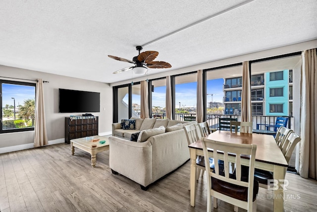 living room with light wood finished floors, ceiling fan, baseboards, and a textured ceiling