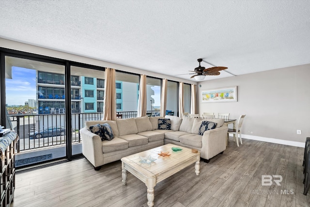 living area with a ceiling fan, a textured ceiling, baseboards, and wood finished floors