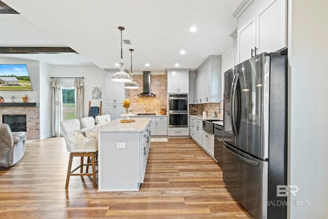 kitchen with a kitchen breakfast bar, light hardwood / wood-style flooring, a center island, stainless steel appliances, and wall chimney range hood