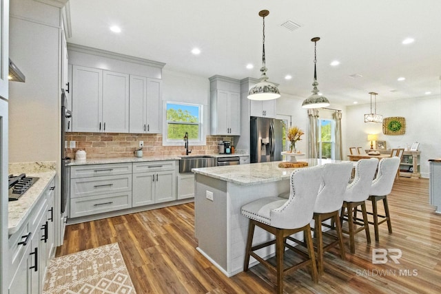 kitchen with decorative light fixtures, a center island, sink, appliances with stainless steel finishes, and hardwood / wood-style flooring