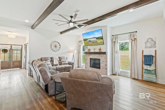 living room featuring a fireplace, wood-type flooring, beam ceiling, and ceiling fan