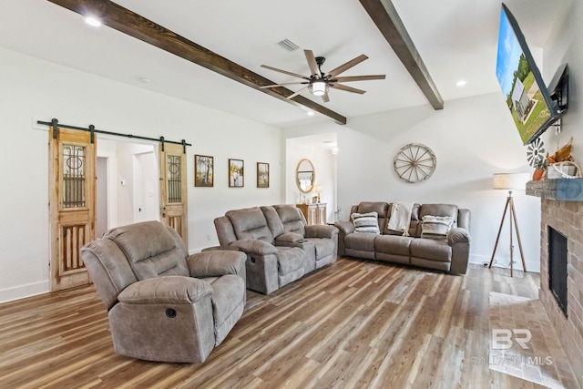 living room with a fireplace, a barn door, hardwood / wood-style floors, ceiling fan, and beam ceiling