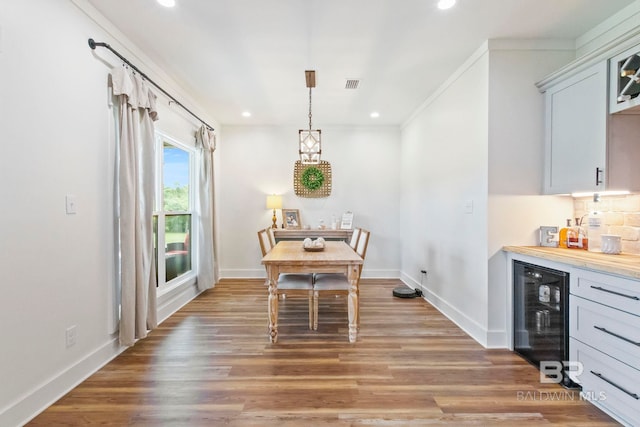 dining space with bar, hardwood / wood-style floors, wine cooler, and ornamental molding