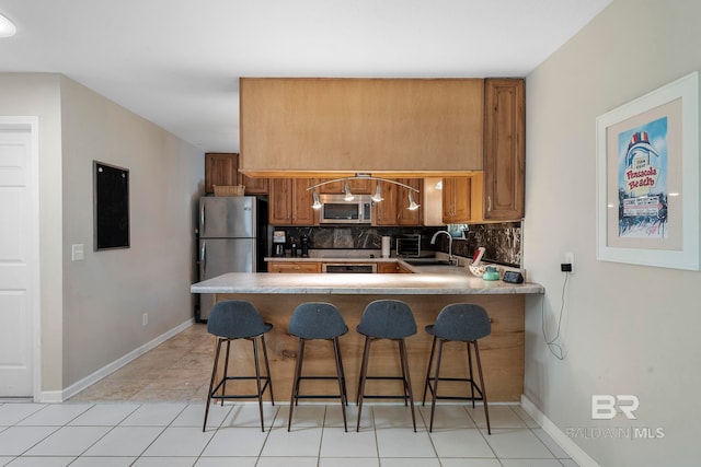 kitchen featuring a breakfast bar, sink, kitchen peninsula, stainless steel appliances, and decorative backsplash