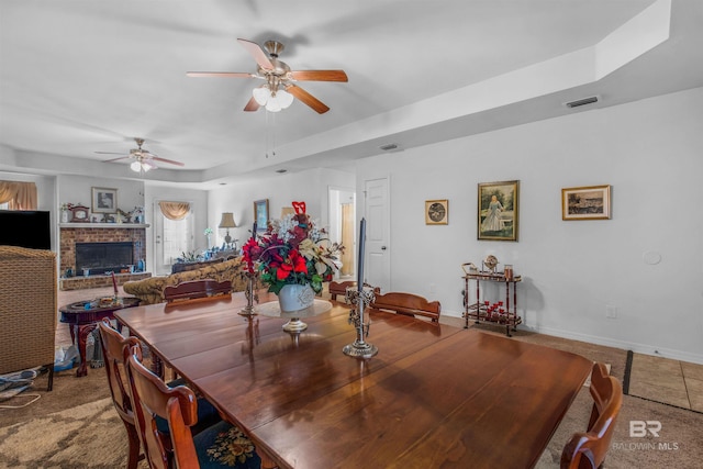 dining area featuring a brick fireplace, ceiling fan, and a tray ceiling