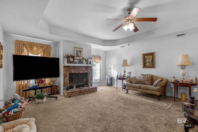 living room with a raised ceiling, ceiling fan, carpet, and a brick fireplace