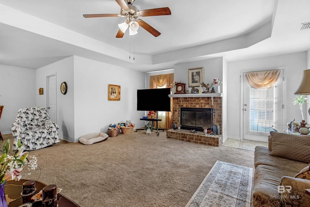 carpeted living room featuring a fireplace, a tray ceiling, and ceiling fan