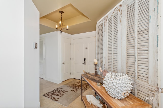 hallway featuring a chandelier, light tile flooring, and a raised ceiling