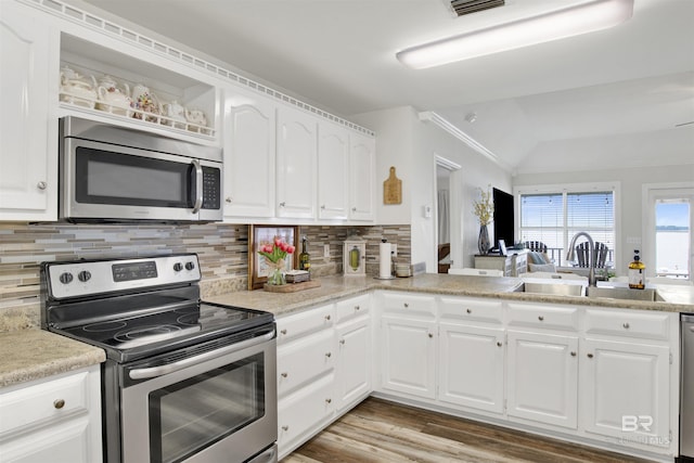kitchen featuring backsplash, appliances with stainless steel finishes, white cabinets, a sink, and wood finished floors