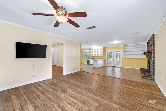 unfurnished living room featuring hardwood / wood-style floors, ornamental molding, french doors, and a brick fireplace