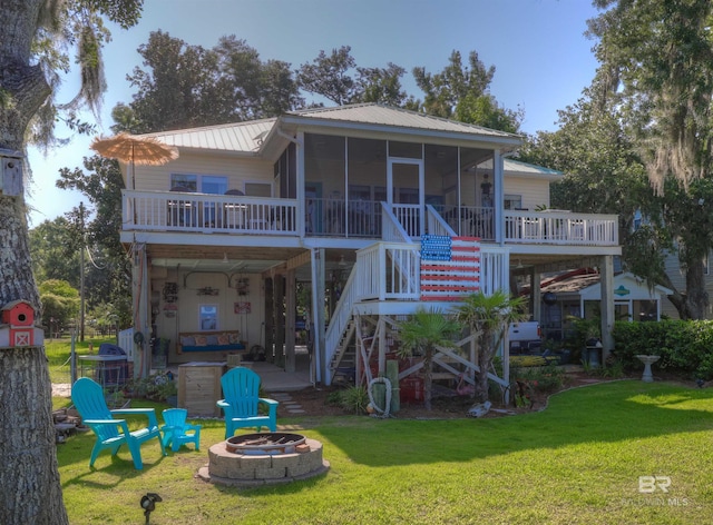 rear view of house featuring a fire pit, a lawn, and a sunroom