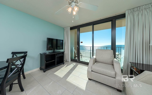 living room with ceiling fan, a wall of windows, a water view, light tile floors, and a textured ceiling