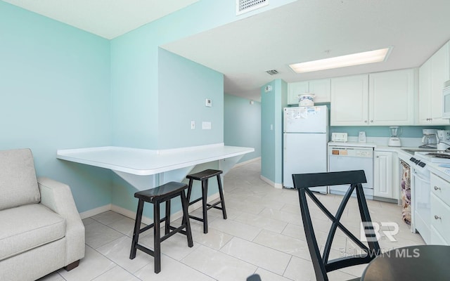 kitchen with white appliances, a breakfast bar, white cabinets, and light tile floors