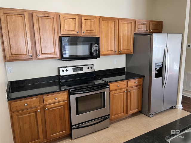 kitchen with light tile patterned flooring, appliances with stainless steel finishes, and dark stone countertops