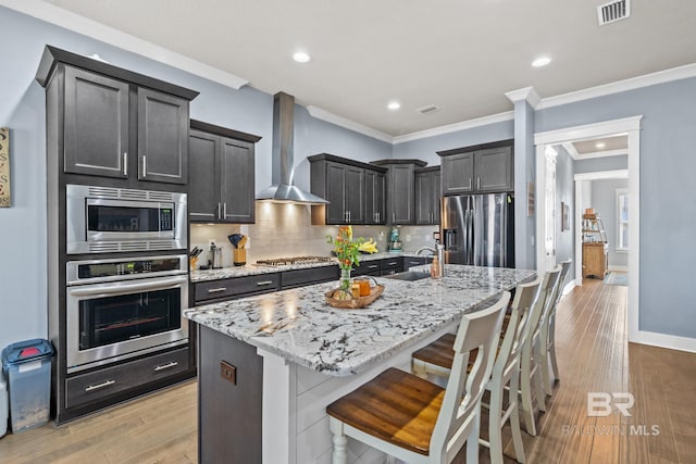 kitchen with visible vents, a sink, appliances with stainless steel finishes, wall chimney exhaust hood, and backsplash