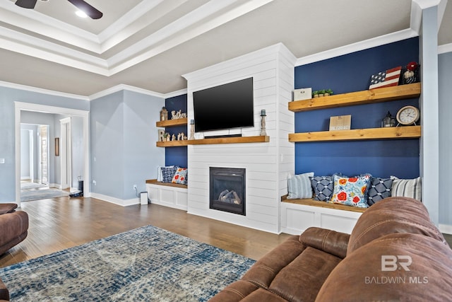 living area featuring a large fireplace, crown molding, baseboards, a tray ceiling, and wood finished floors