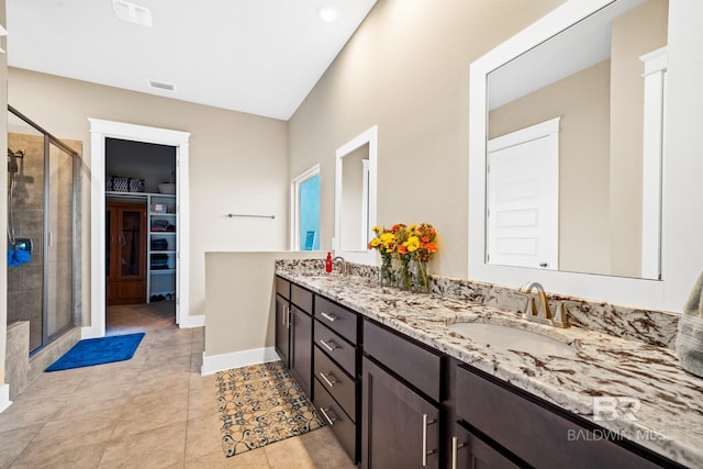 bathroom featuring visible vents, double vanity, a sink, a shower stall, and a walk in closet