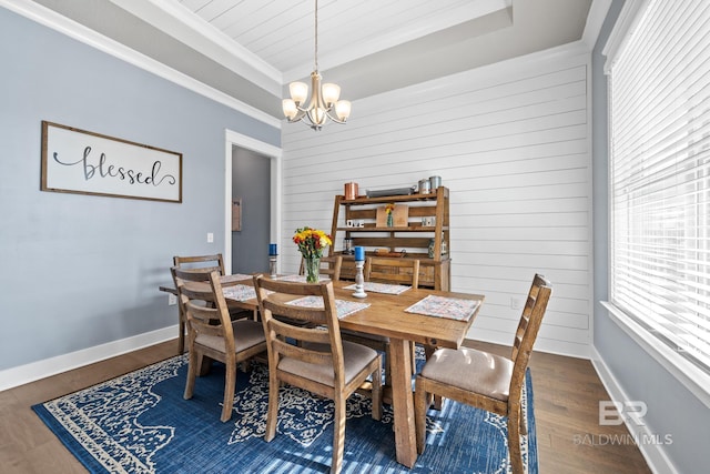 dining space featuring a notable chandelier, a tray ceiling, wood finished floors, crown molding, and baseboards