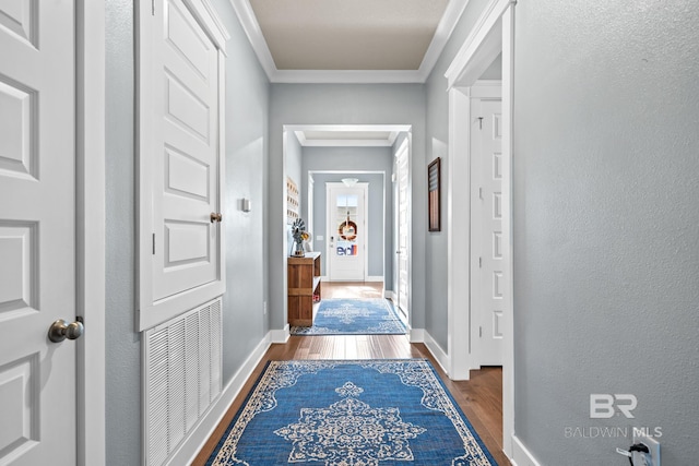 corridor with visible vents, wood finished floors, baseboards, and ornamental molding