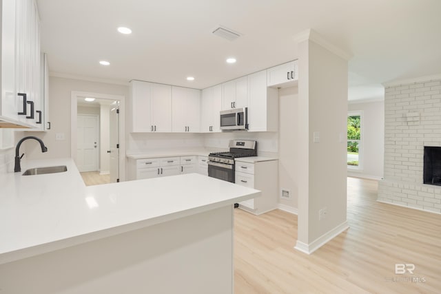 kitchen with white cabinetry, sink, stainless steel appliances, light hardwood / wood-style flooring, and kitchen peninsula