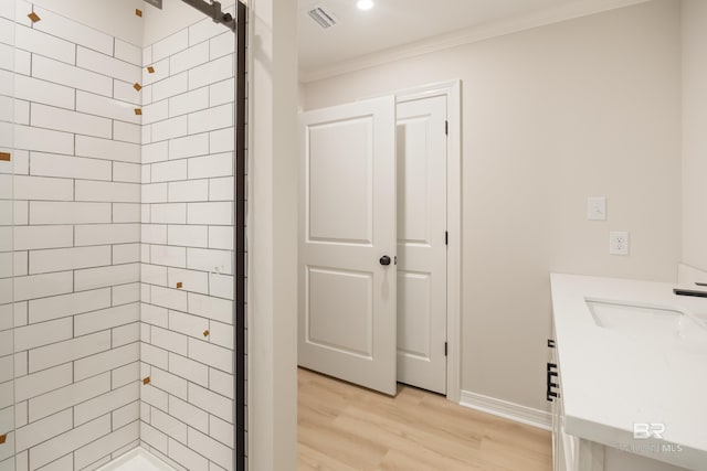 bathroom with wood-type flooring, vanity, a tile shower, and crown molding