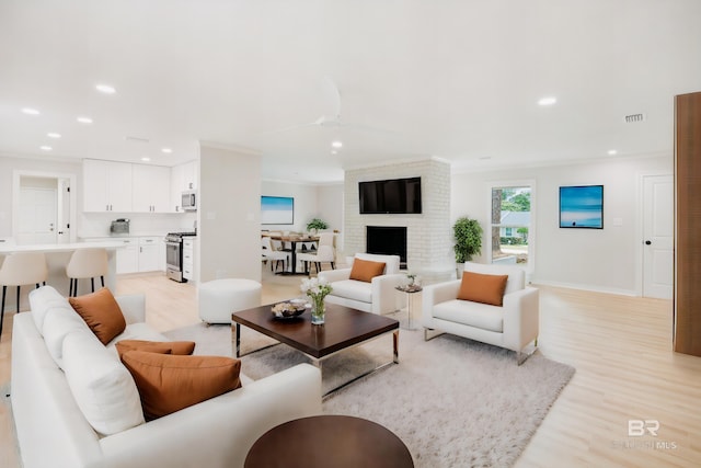 living room featuring crown molding, ceiling fan, light hardwood / wood-style floors, and a brick fireplace