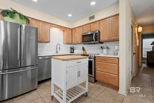 1069 W Beach Blvd Unit 5C, Gulf Shores, AL 36542 - kitchen with appliances with stainless steel finishes, decorative backsplash, a textured ceiling, light tile patterned floors, and a center island
