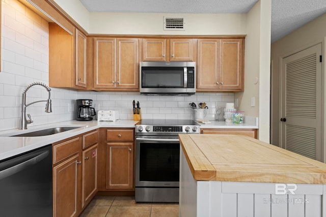 1069 W Beach Blvd Unit 5C, Gulf Shores, AL 36542 - kitchen with appliances with stainless steel finishes, wood counters, decorative backsplash, and brown cabinets