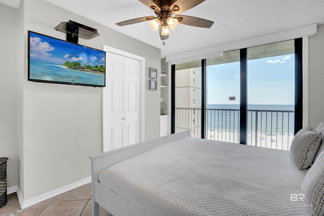 bedroom featuring access to outside, light tile patterned flooring, a water view, and a textured ceiling