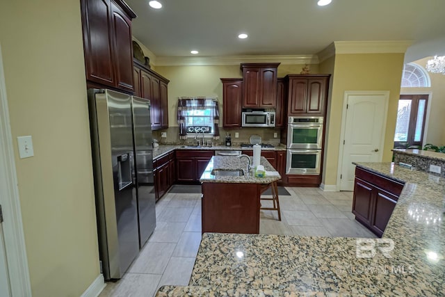 kitchen featuring a kitchen island with sink, light stone countertops, tasteful backsplash, appliances with stainless steel finishes, and a kitchen bar