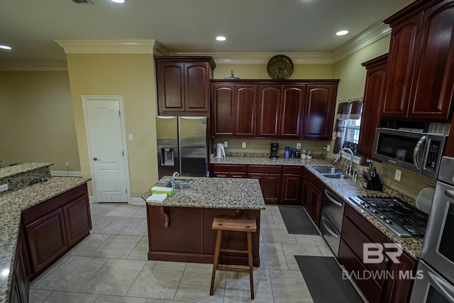 kitchen featuring appliances with stainless steel finishes, light stone countertops, a breakfast bar, a kitchen island, and sink