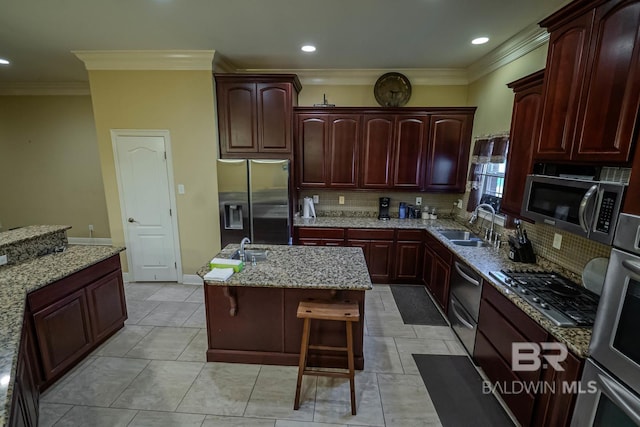 kitchen featuring stainless steel appliances, a kitchen island, light stone countertops, ornamental molding, and a breakfast bar area