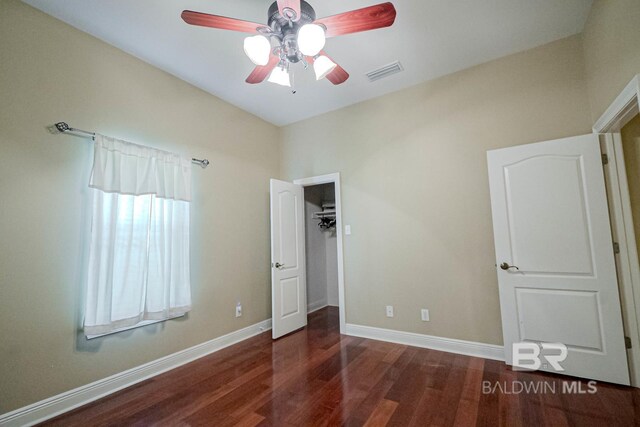 unfurnished bedroom featuring ceiling fan, dark wood-type flooring, and a walk in closet