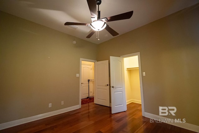 unfurnished bedroom featuring dark hardwood / wood-style flooring, ceiling fan, a walk in closet, and a closet