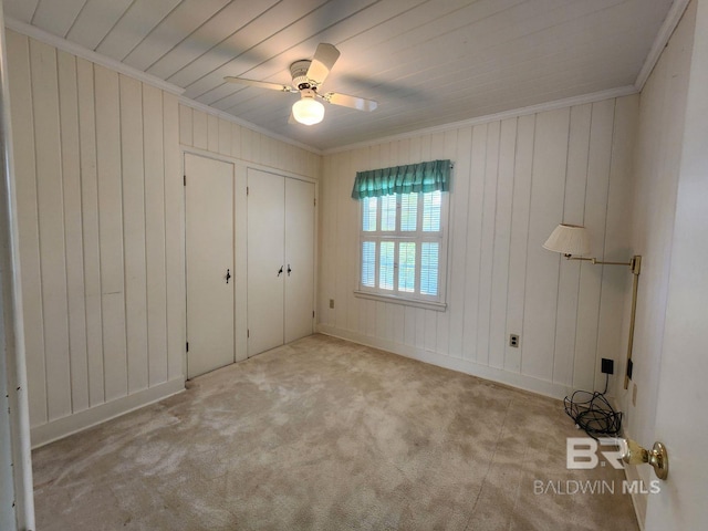 unfurnished bedroom featuring light carpet, wooden walls, ceiling fan, and crown molding