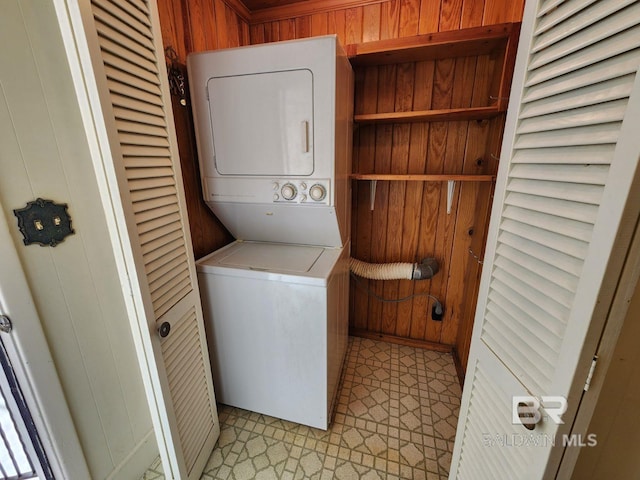 laundry area featuring wooden walls and stacked washer and dryer