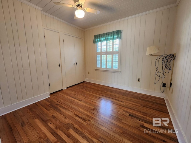 unfurnished bedroom with ceiling fan, wooden walls, crown molding, and hardwood / wood-style floors