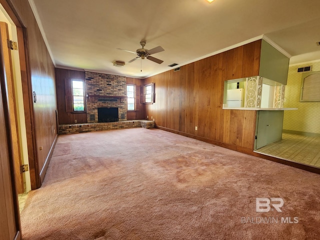 unfurnished living room with ceiling fan, wood walls, carpet flooring, ornamental molding, and a brick fireplace