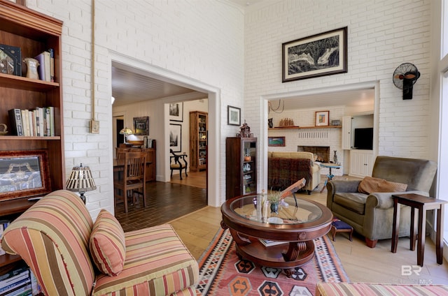 living room with a fireplace, a towering ceiling, brick wall, and wood finished floors