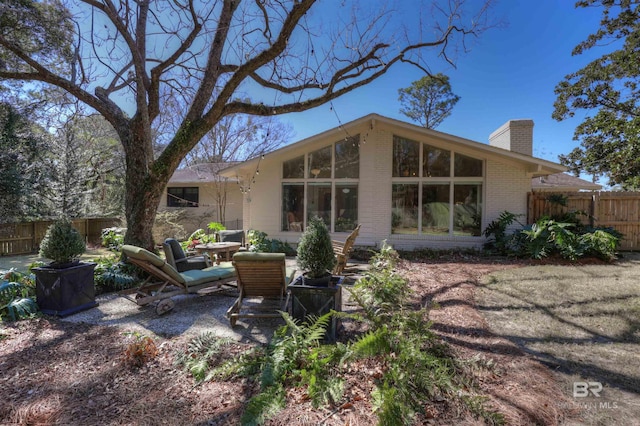 back of house featuring a patio, brick siding, a chimney, and fence