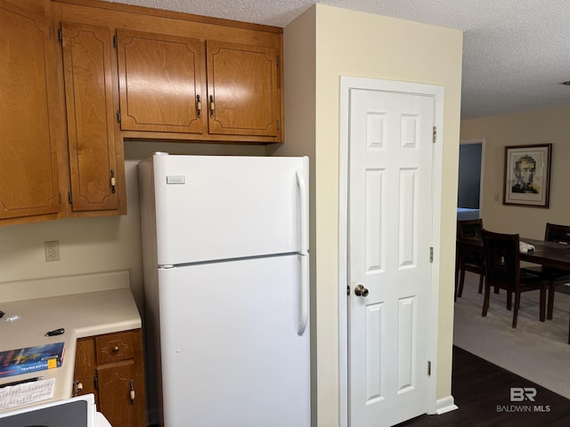 28712 Canal Rd, Orange Beach, AL 36561 - kitchen featuring freestanding refrigerator, brown cabinetry, light countertops, a textured ceiling, and dark wood-type flooring