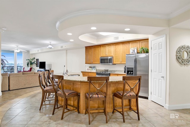 kitchen featuring crown molding, light stone countertops, stainless steel appliances, sink, and a breakfast bar area