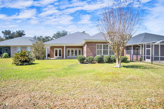 back of property with brick siding, a lawn, french doors, and roof with shingles