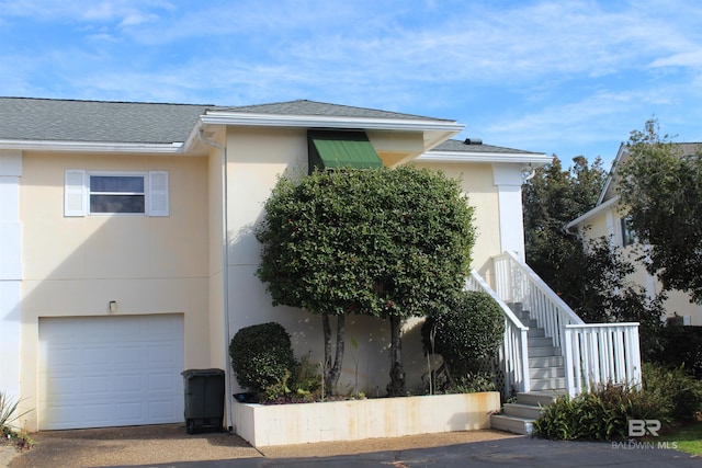 view of front of home with stairs, a garage, a shingled roof, and stucco siding