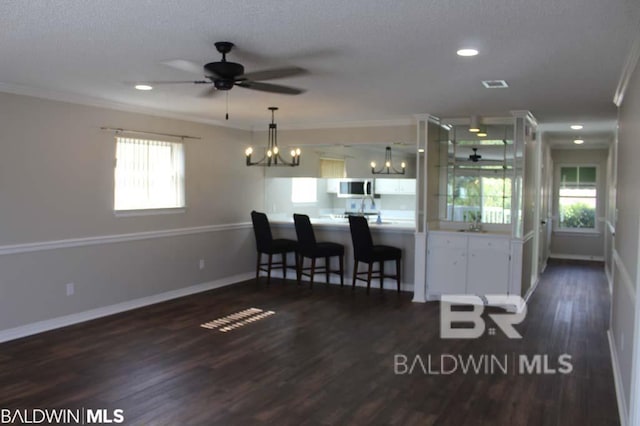 interior space with baseboards, dark wood-style flooring, crown molding, and ceiling fan with notable chandelier